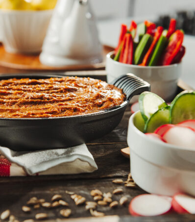 Roasted Red Pepper Dip served in a cast iron skillet with a side of sliced veggies