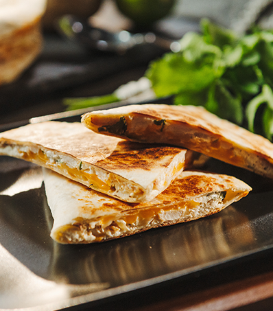 A quesadilla that has been cut into three triangles is stacked on a black circular plate.